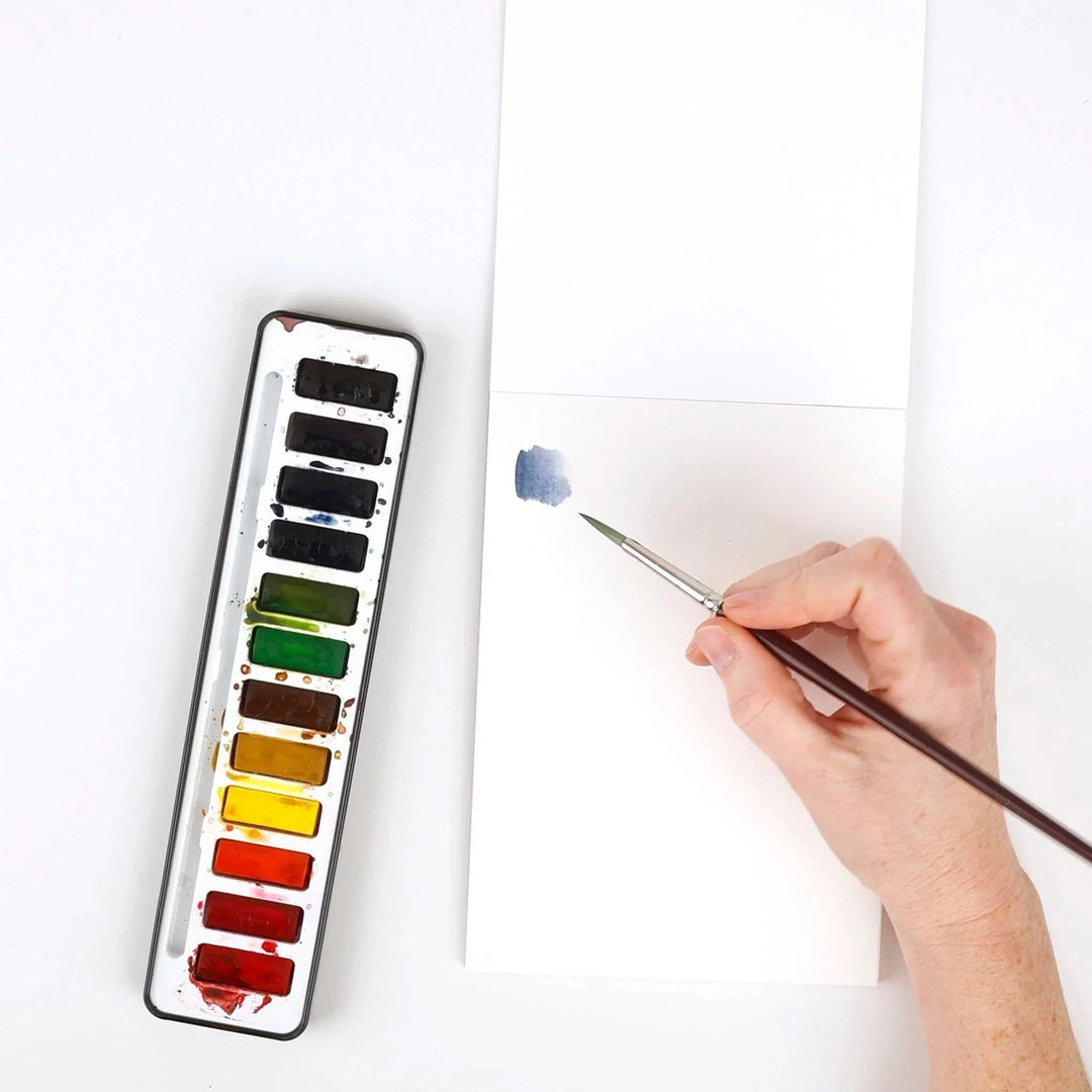 Watercolor paint set with a hand holding a brush and painting on paper.