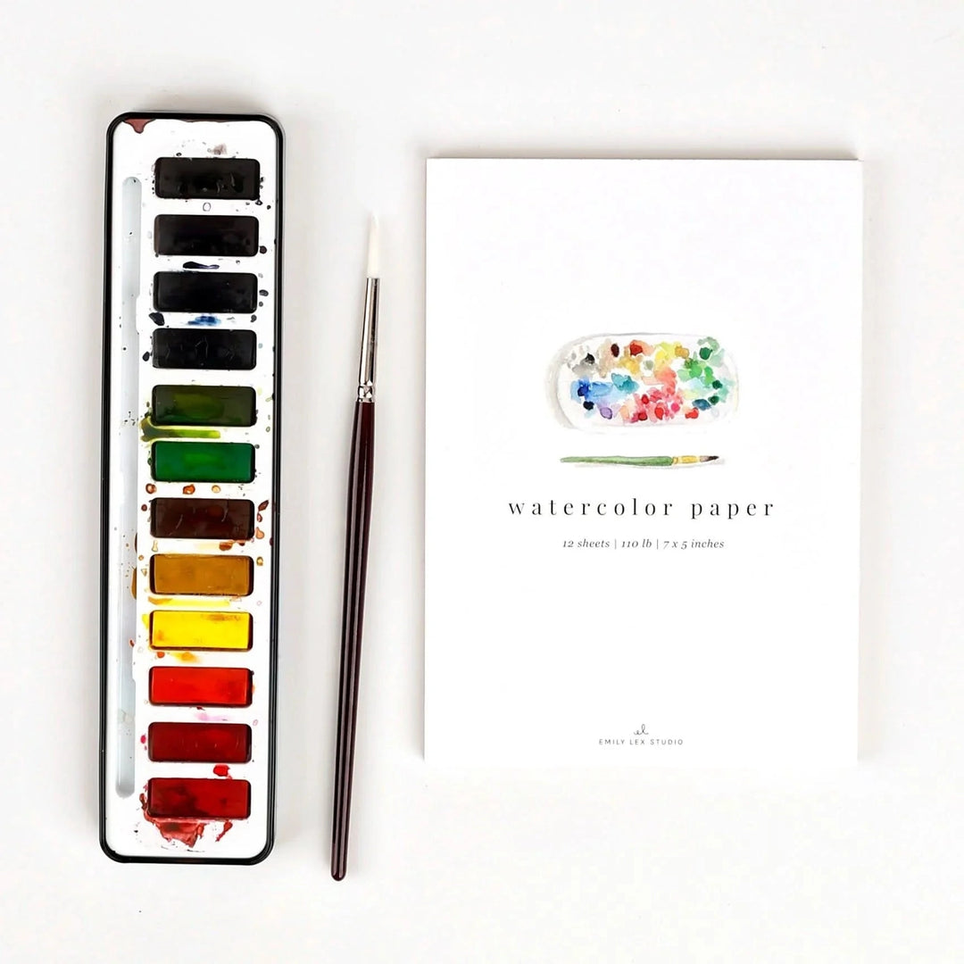 Set of watercolor paints, brush, and watercolor paper on a white background