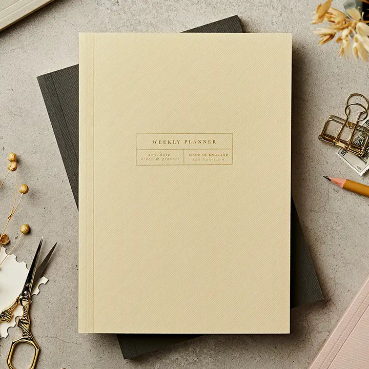 Beige weekly planner notebook on a textured surface with scissors and flowers.