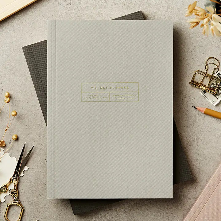 Gray planner with gold text on a light gray surface with office supplies.