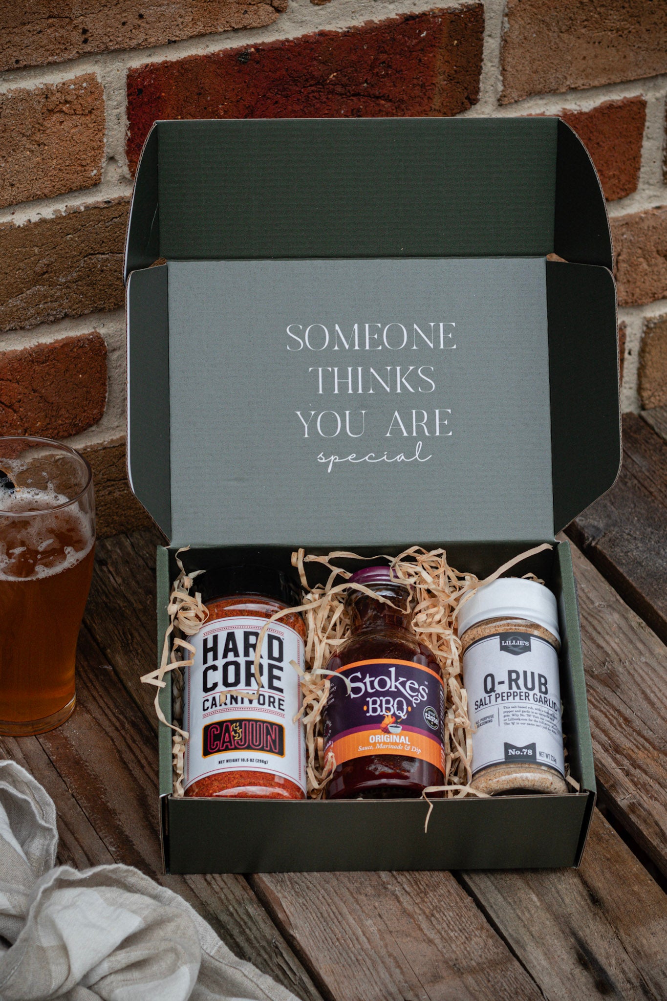 Gift box with barbecue products on a wooden surface against a brick wall.
