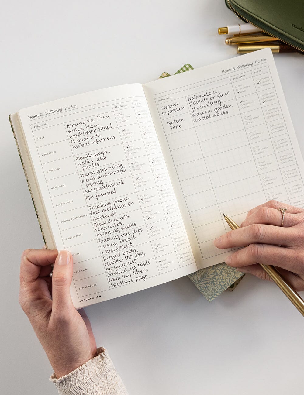 Person writing in a planner with a gold pen on a light surface