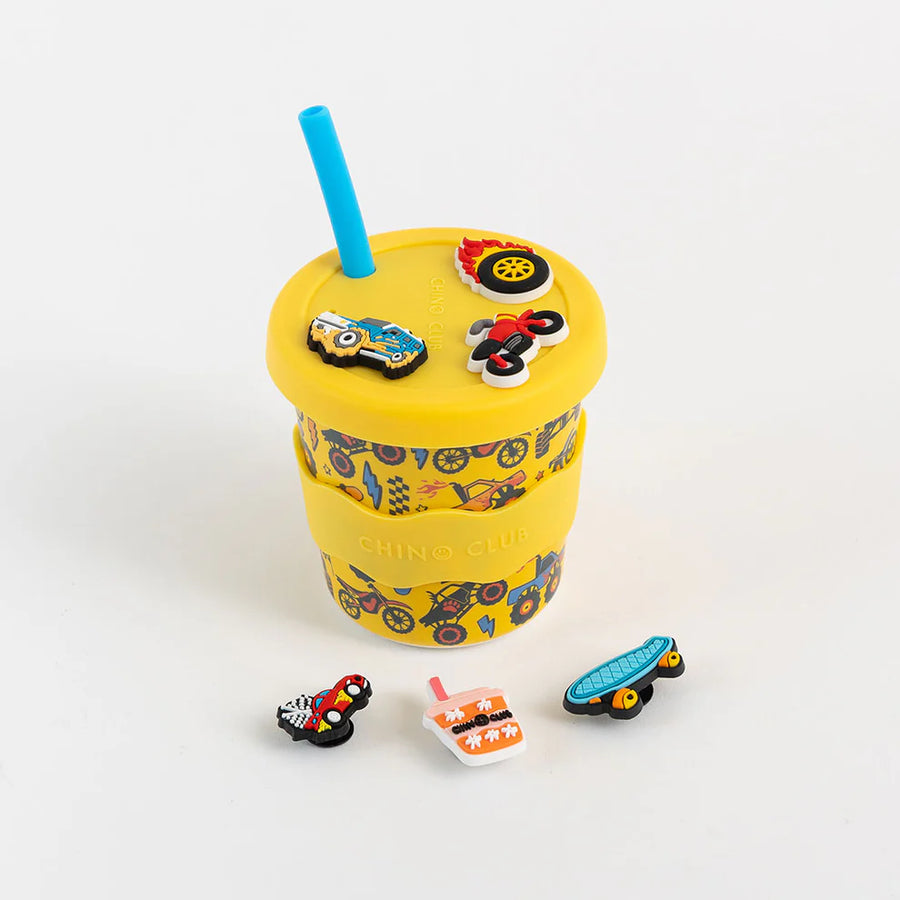 Yellow cup with colorful car-shaped drink charms and a blue straw on a white background