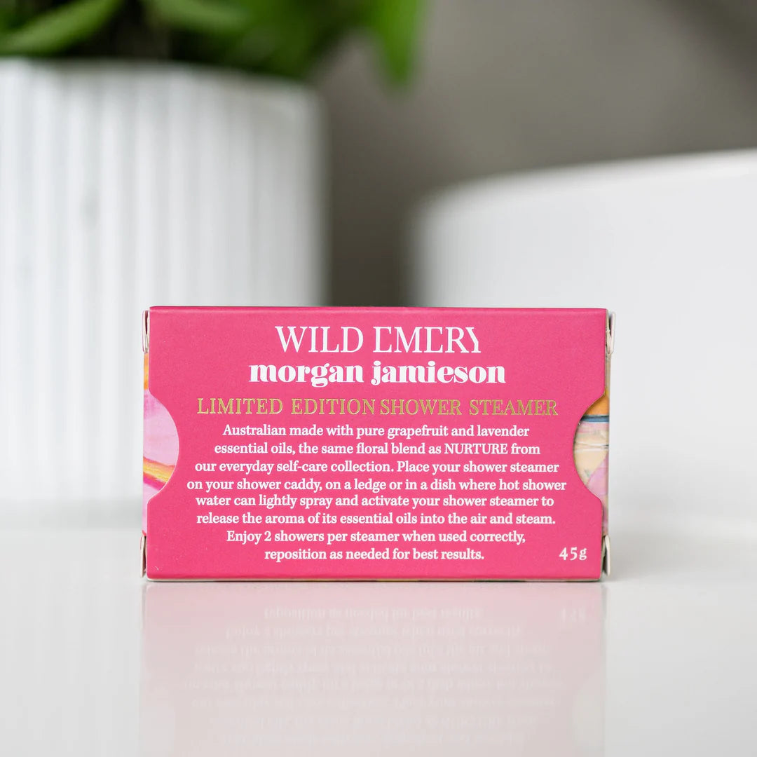 Pink shower steamer packaging with 'Wild Emery Morgan Jameson' branding on a blurred background.