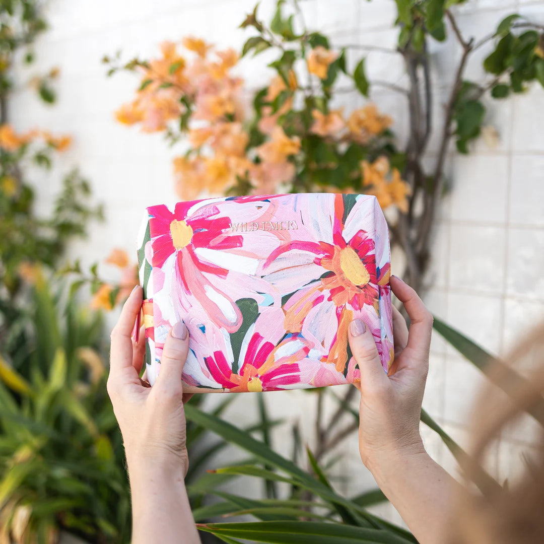 Person holding a floral-patterned cosmetic bag with plants in the background