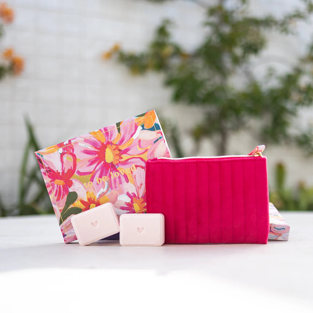 Pink zip pouch with a floral gift box and 2 shower steamers on a white surface