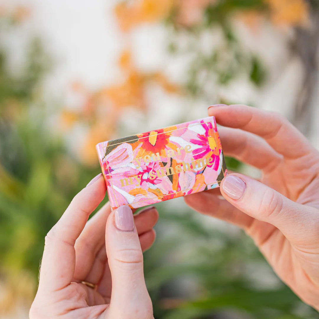 Hand holding a colorful box with floral design against a blurred natural background