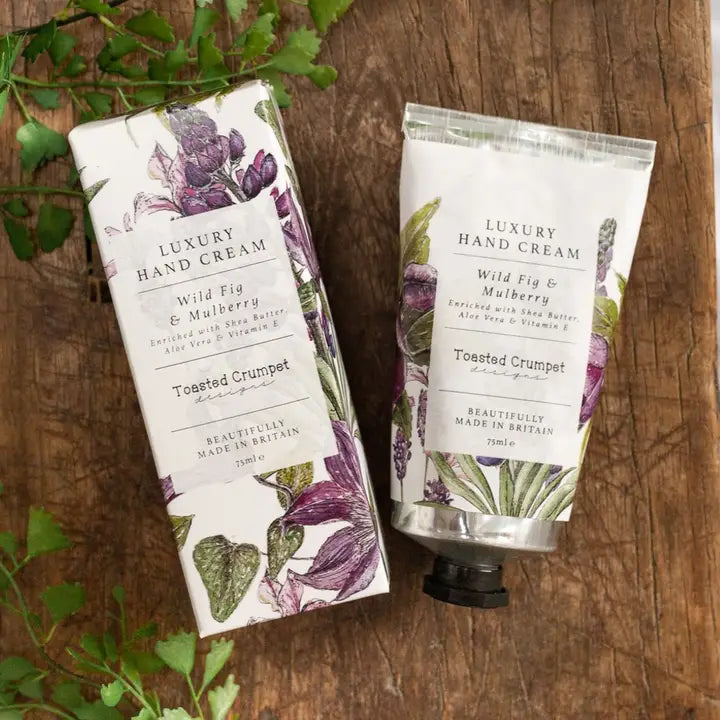 Two luxury hand cream containers on a wooden surface with green leaves.
