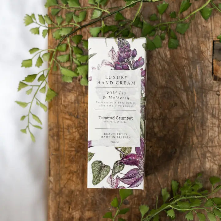 Luxury hand cream packaging with floral design on a wooden surface with green leaves.