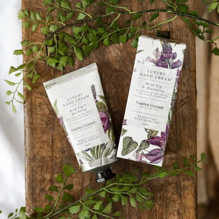 Two luxury hand cream containers on a wooden board with green leaves.