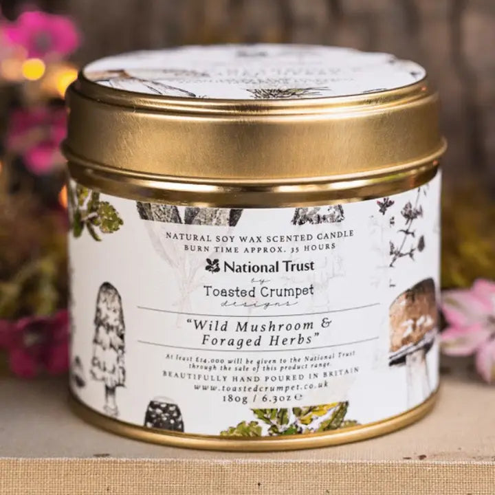 Candle in a tin with a decorative label featuring mushrooms and herbs, branded as 'National Trust'.