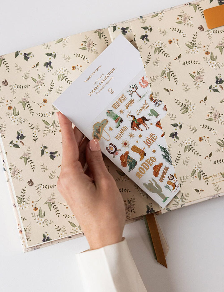 Hand holding a small book with stickers on a larger book with a floral pattern