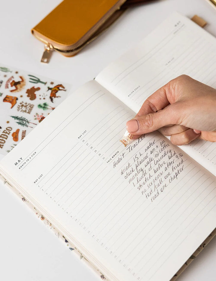 Hand writing in a notebook with a decorative pen on a white surface