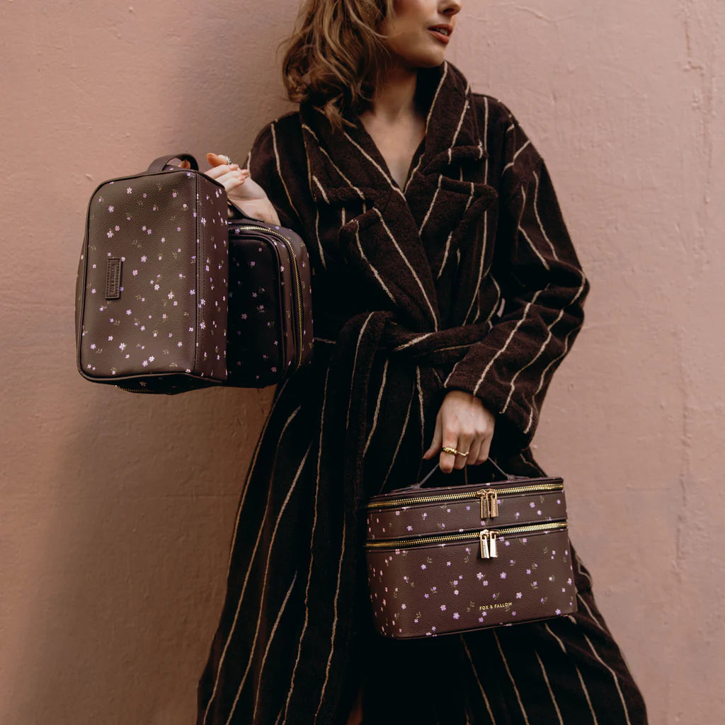 Person holding a brown patterned cosmetic bag against a plain background