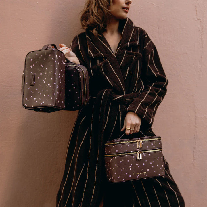 Person holding a brown patterned cosmetic bag against a plain background