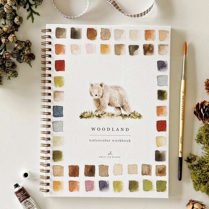 Notebook titled 'Woodland Watercolor Workbook' with a bear illustration on a color swatch background.