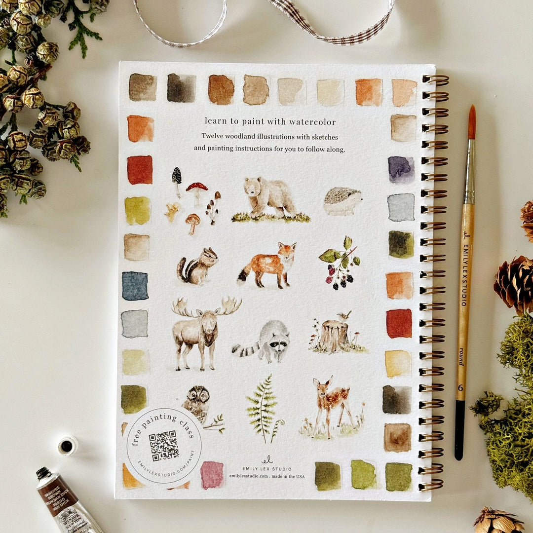 Notebook with nature-themed illustrations and color swatches on a white surface with art supplies.