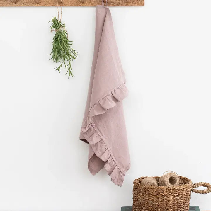Light pink linen tea towel with a ruffle hanging on a hook