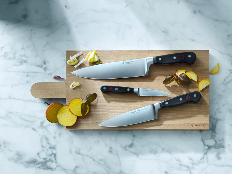 Set of knives on a wooden cutting board with sliced apples on a marble surface