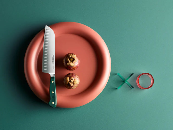 Wusthof santoku Knife on a red plate with two apples and a green &
