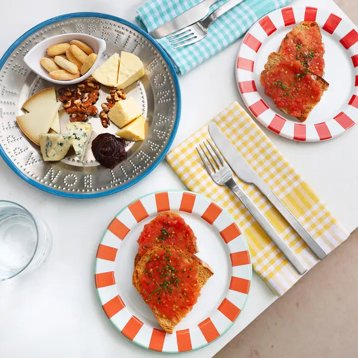 Plates of food with striped plates and checkered napkins on a table.
