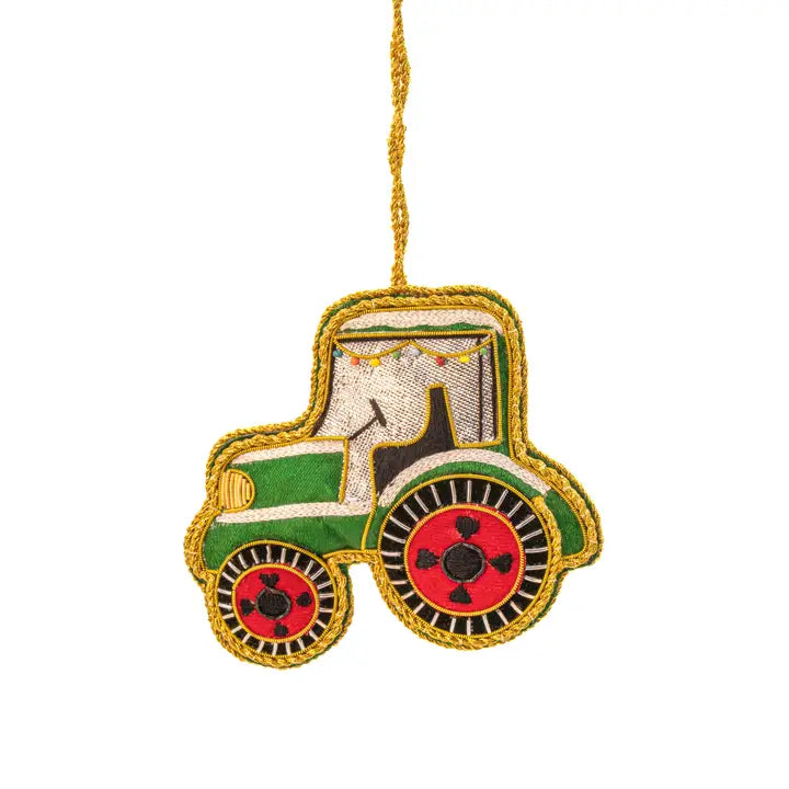 A decorative embroidered tractor ornament with a gold hanging string, featuring green and cream fabric with red wheels and black details, set against a plain white background.