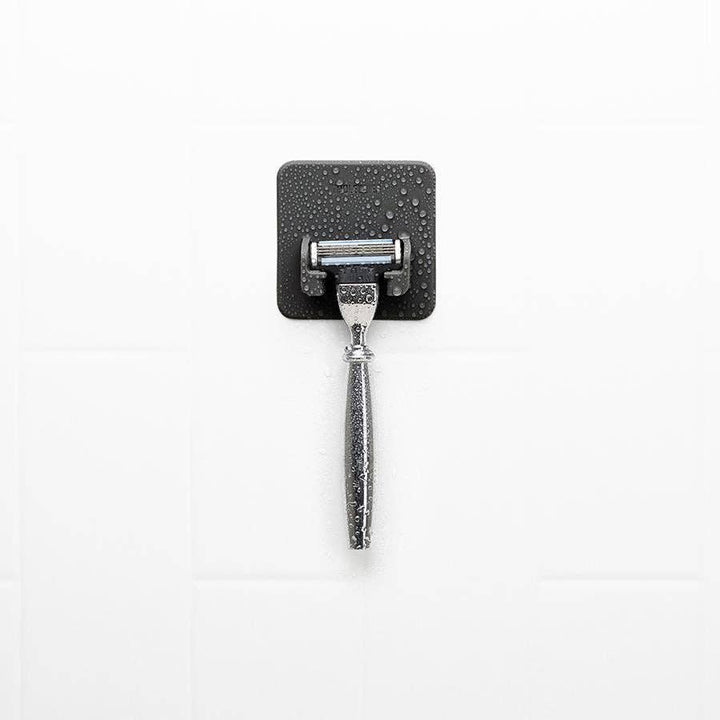 Grey silicone razor holder stuck to a white tiled wall, holding a razor