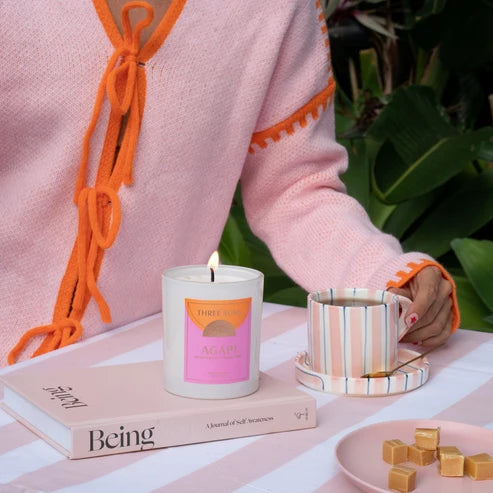 Person holding a mug with a lit candle and books on a table