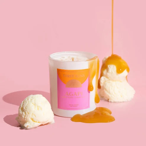 A white candle jar with a pink and orange label reading &