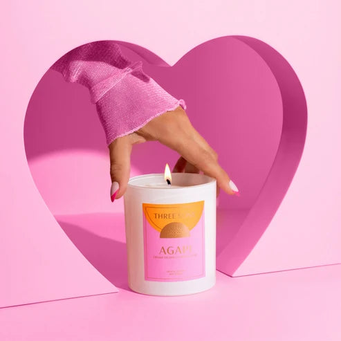 Candle with a pink label held by a hand against a heart-shaped pink background