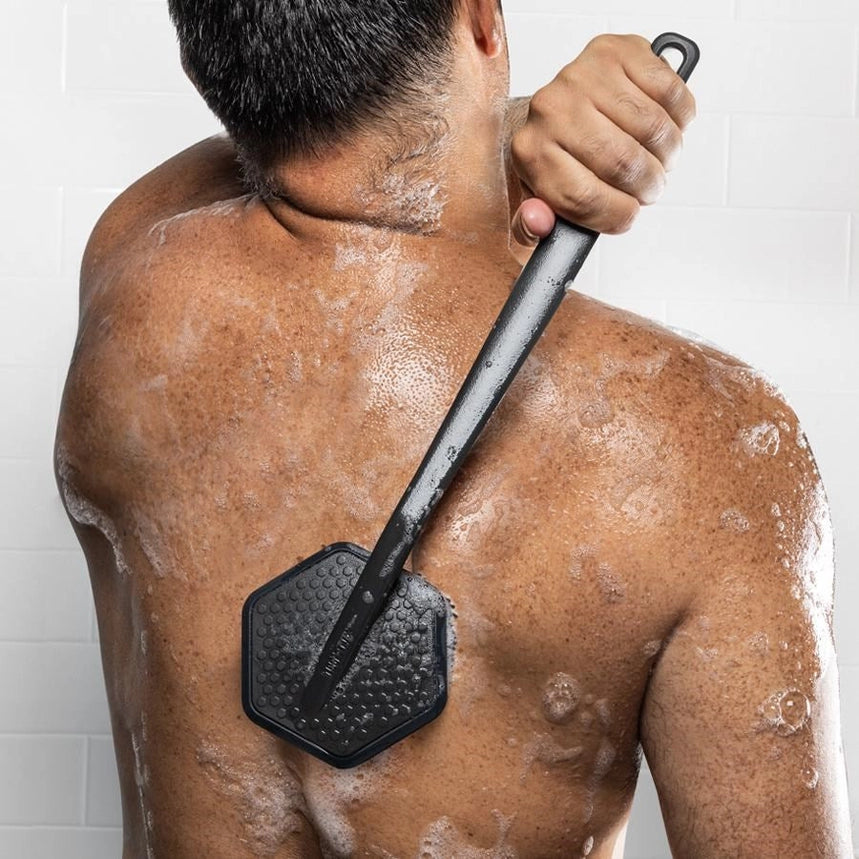 Person using a black skin exfoliating tool on their back with soap suds.