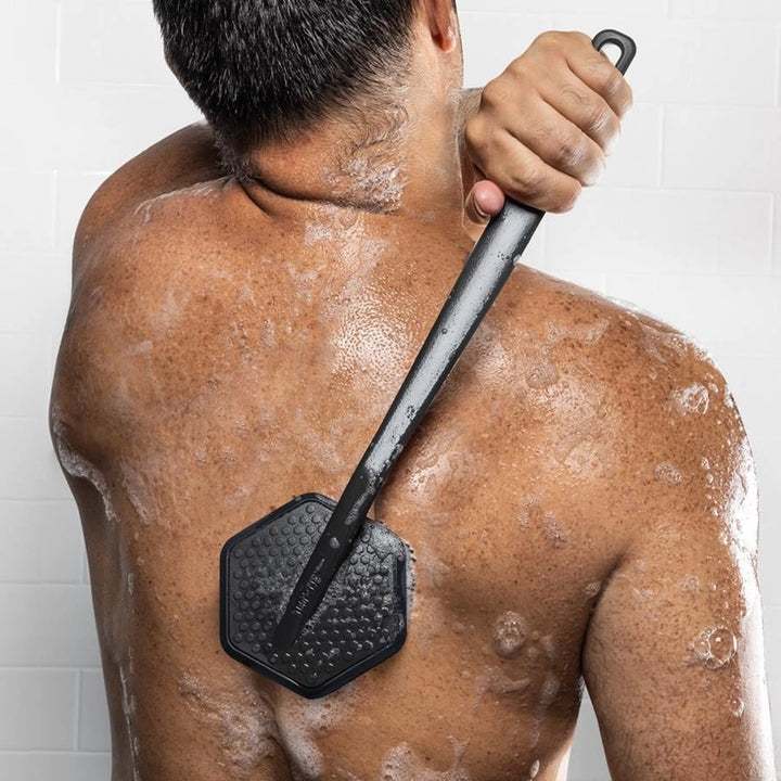 Person using a black skin exfoliating tool on their back with soap suds.