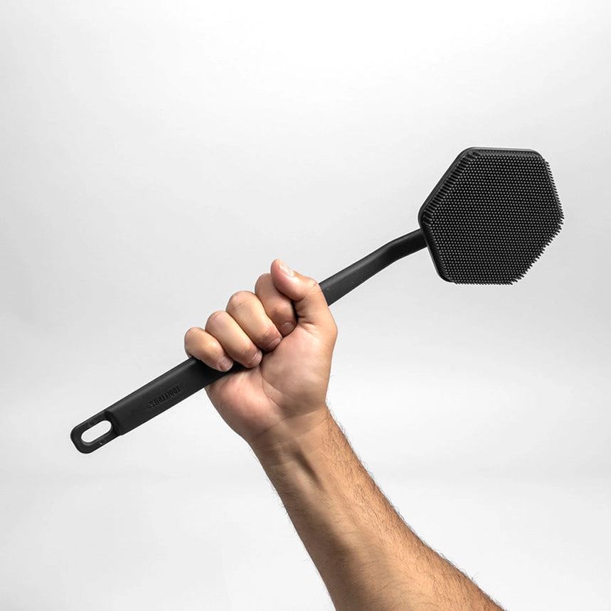 Hand holding a charcoal coloured silicone back scrubber in front of a white background