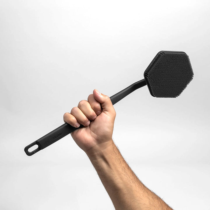 Hand holding a charcoal coloured silicone back scrubber in front of a white background