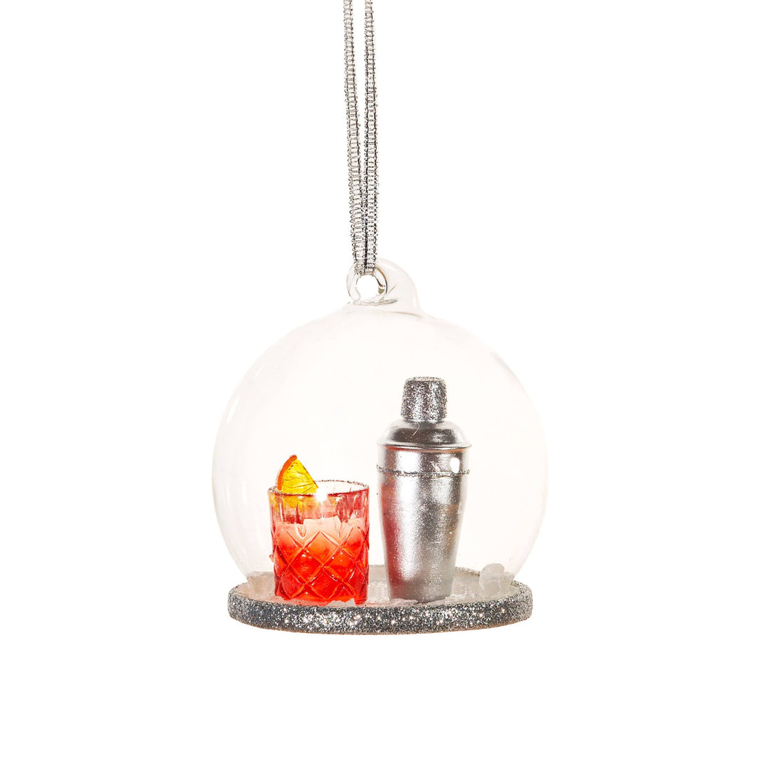 A clear spherical hanging ornament with a silver glitter base, featuring a miniature red cocktail glass with a yellow garnish and a silver shaker inside, suspended by a silver string on a white background.