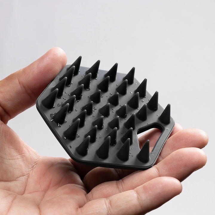 A black silicone beard scrubber with multiple pointed silicone spikes and a built-in handle, held in a person&