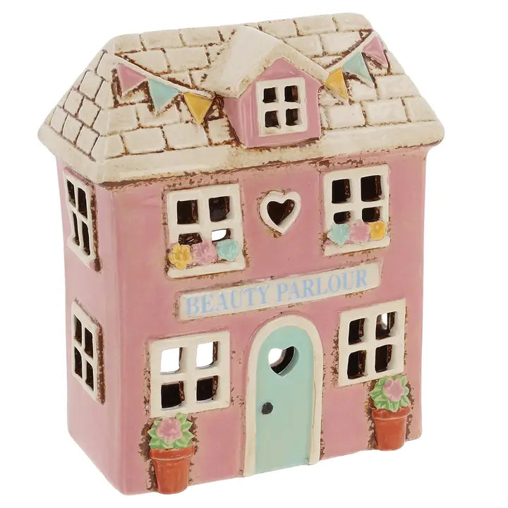 A pink ceramic tealight house with the words Beauty Parlous and flowers & bunting on it on  white background