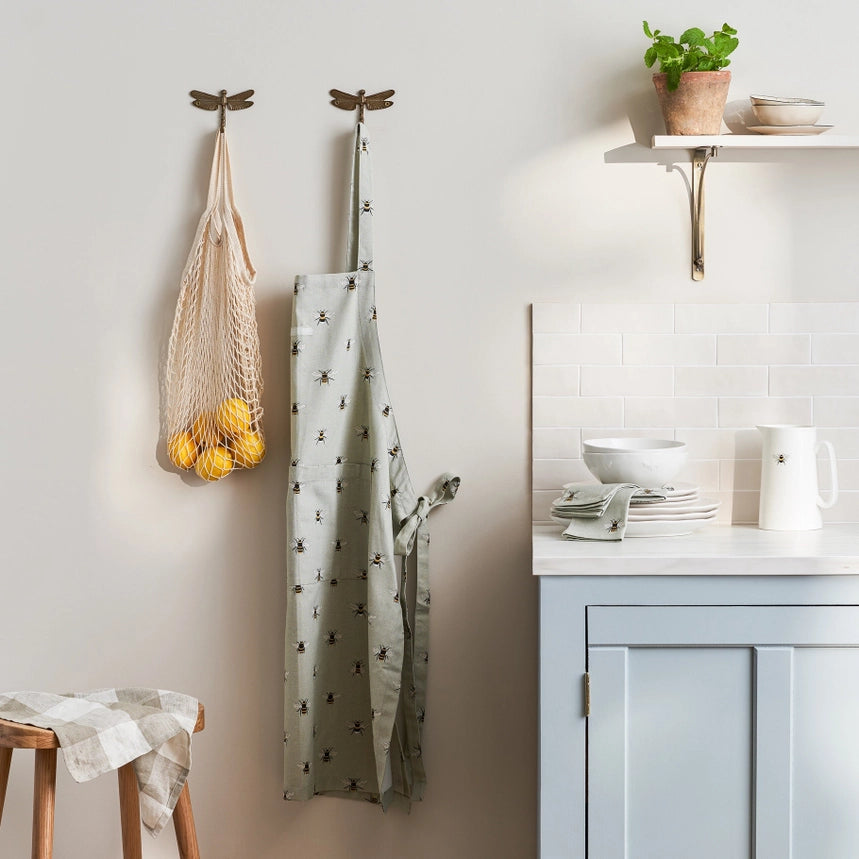 Fabric apron with small bee pattern hanging on a dragonfly shaped hook on a kitchen wall