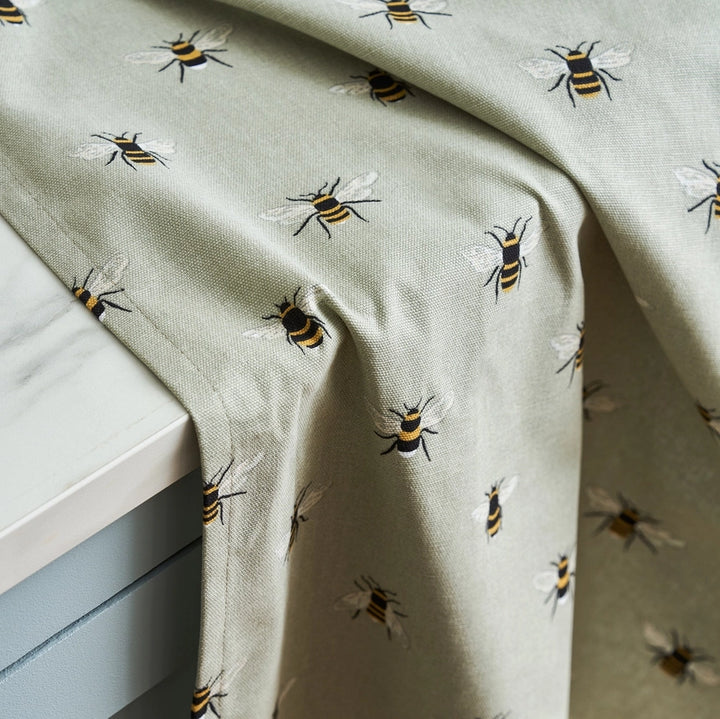 A kitchen tea towel with a hanging loop at the top left, featuring a repeating pattern of small bumblebees draped over a kitchen benchtop