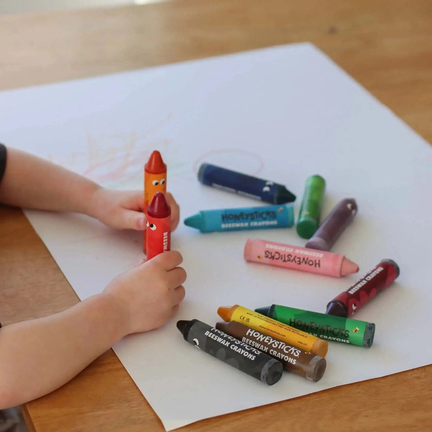 Childs hands holding 2 crayons on paper with more crayons laying on the paper
