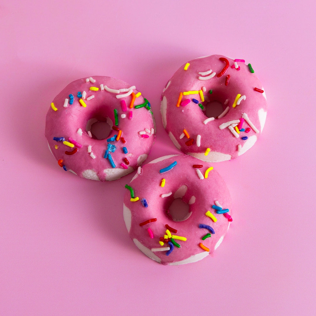 Three pink donuts with colorful sprinkles on a pink background