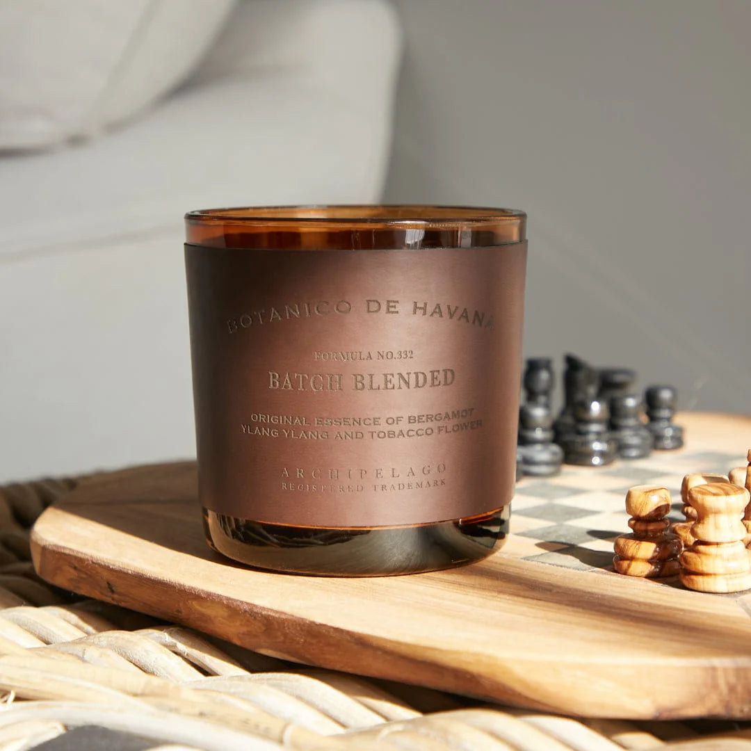 Candle with a brown label on a wooden surface next to chess pieces
