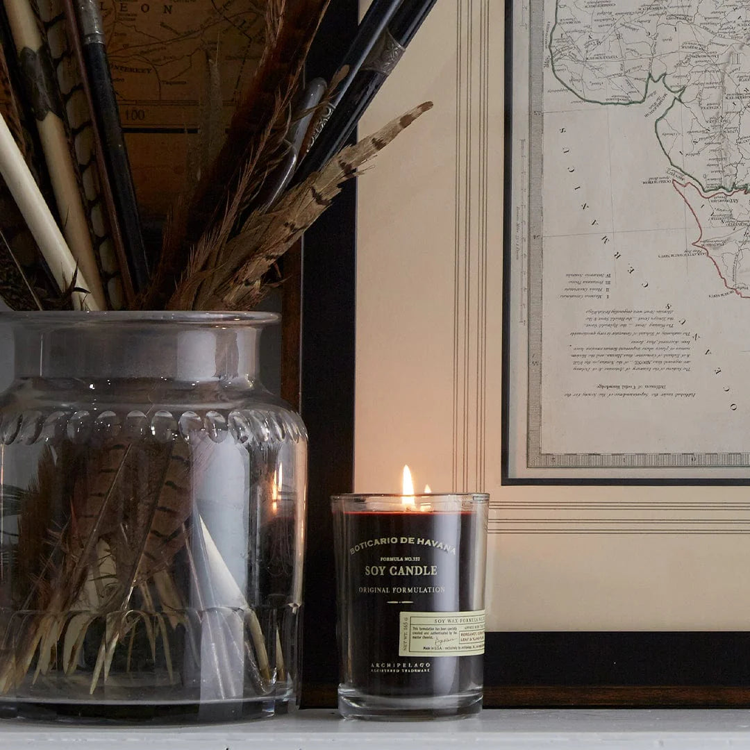 Candle with a decorative jar and feather arrangement on a surface, with a framed map in the background.