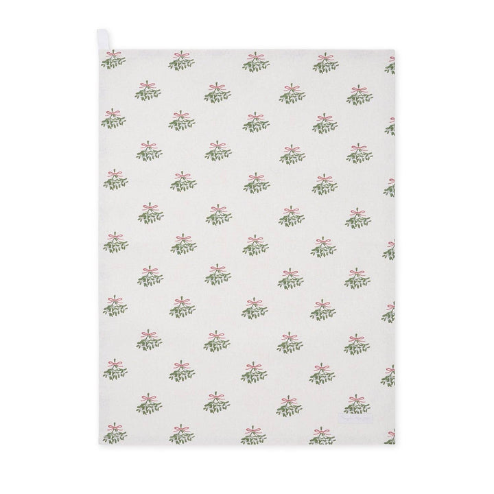 A white kitchen tea towel with a repeating pattern of green mistletoe branches and pink bows, featuring a white hanging loop at the top left corner.