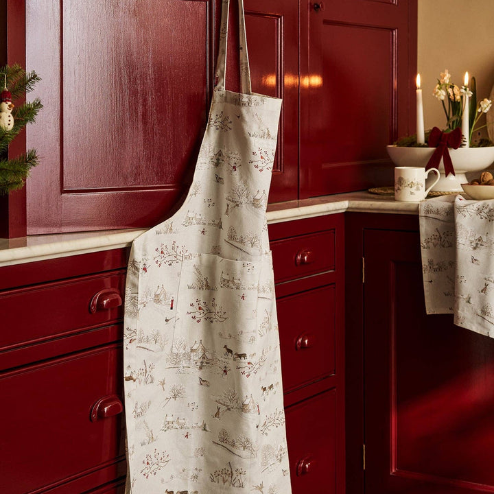 White apron with a Christmas village pattern hanging on a red cabinet in a kitchen.