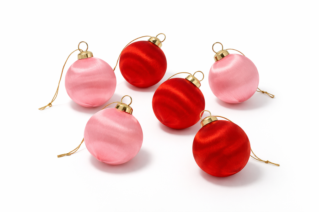 Six round Christmas ornaments with gold caps and hanging loops, featuring a mix of glossy red and soft pink satin finishes, arranged on a clean white background.