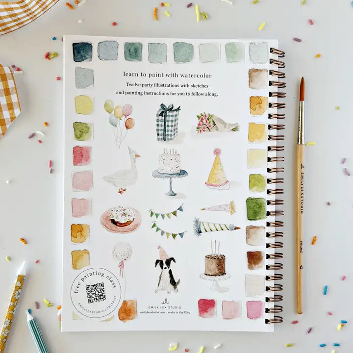 The back page of an Emily Lex celebrate watercolor workbook, on a surface covered in sprinkles and next to a paintbrush.