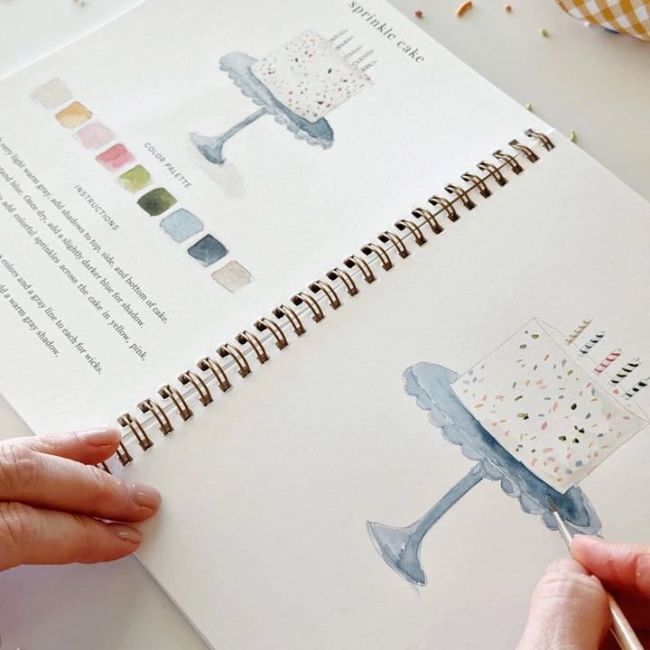 A hand painting a cake on a cake stand