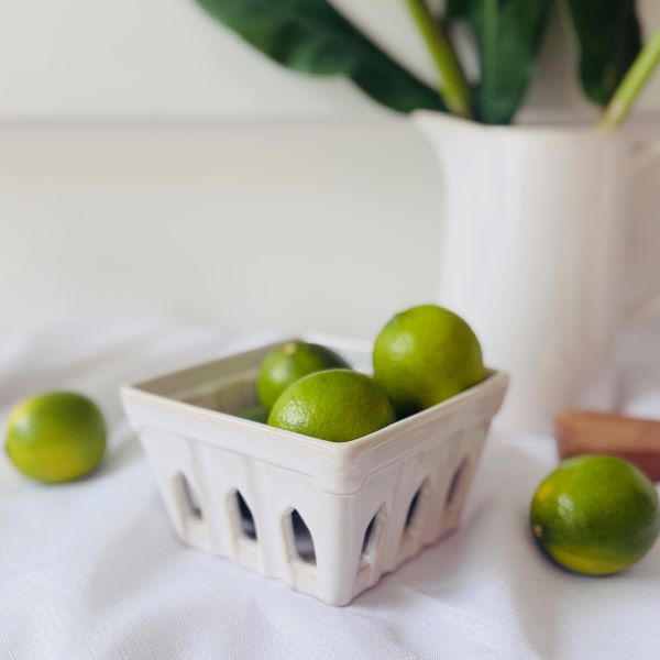 Green limes in a white ceramic punnet on a white surface with a blurred background
