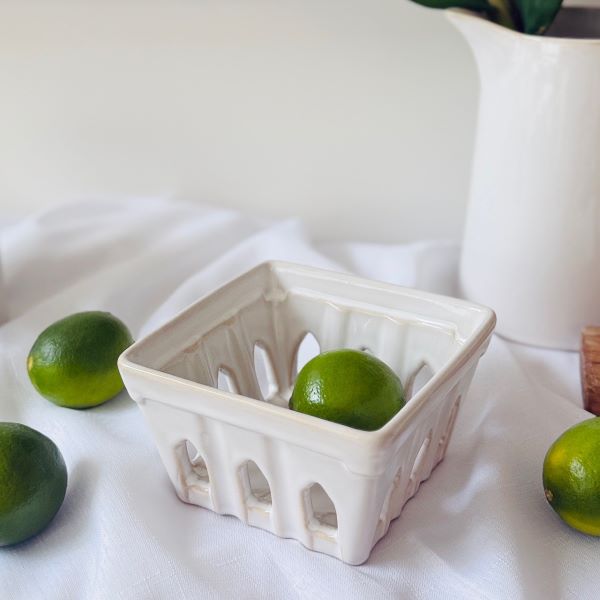 Green limes in a white ceramic punnet on a white surface
